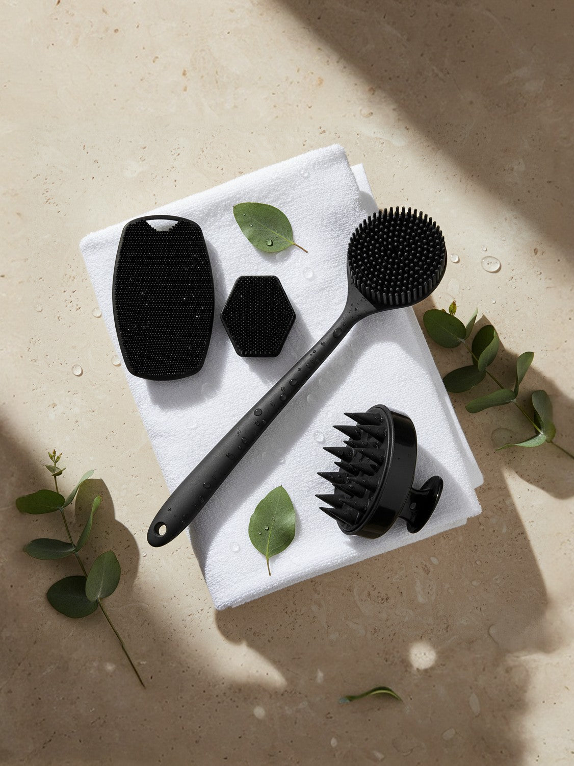 Set of black skin care tools on a white towel with green leaves on a beige surface
