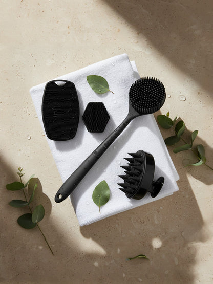 Set of black skin care tools on a white towel with green leaves on a beige surface