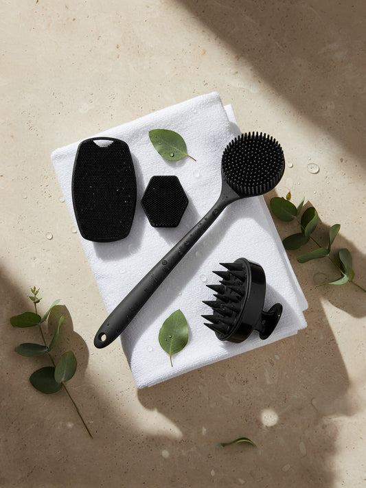 Set of black skin care tools on a white towel with green leaves on a beige surface
